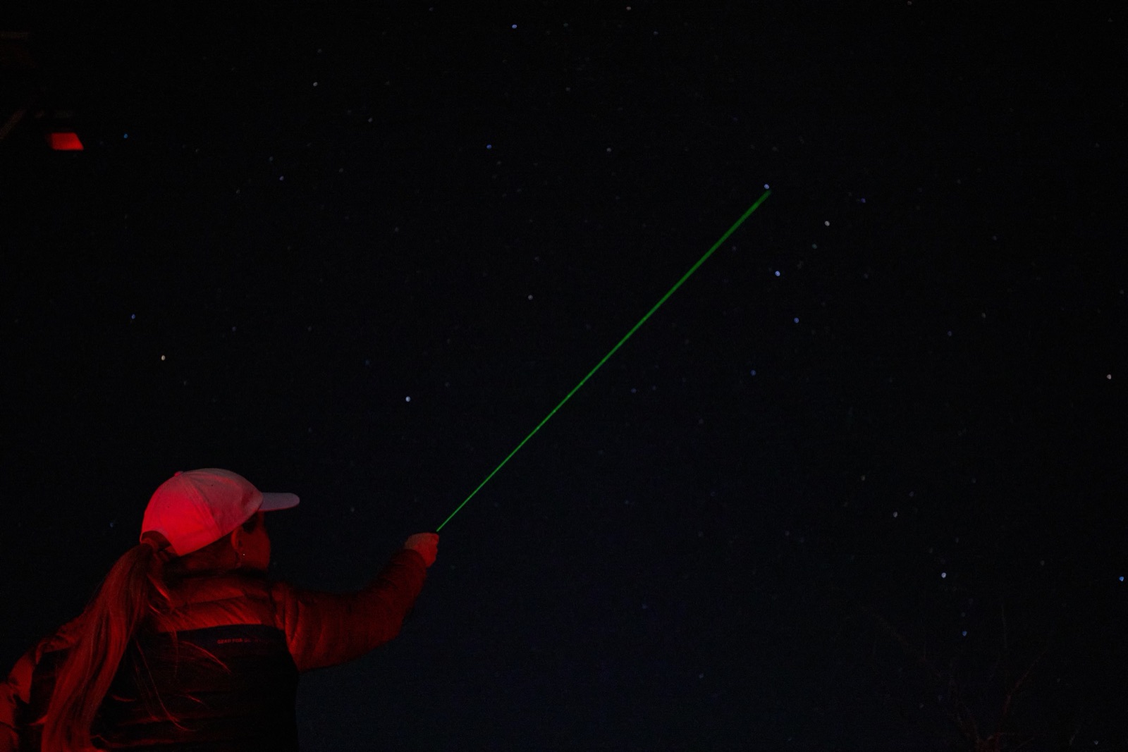Stargazing guide tracing constellations with a green laser pointer under a dark Utah sky