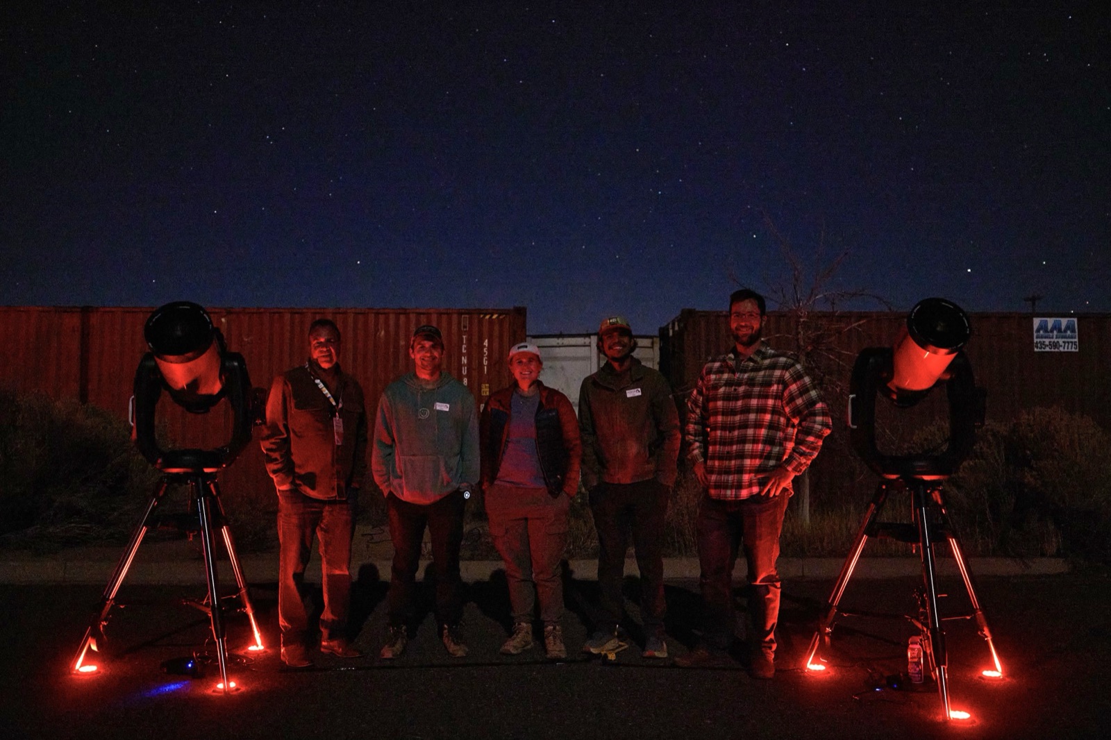 Smiling tour group gathered around telescopes at dusk on a guided Bryce Canyon stargazing tour